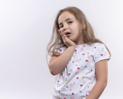 sad little school girl wearing white t-shirt put her hand on aching tooth on isolated white background